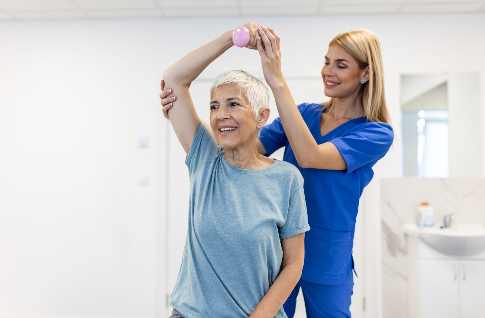 A senior practices a light strength training program under the guidance of a caregiver
