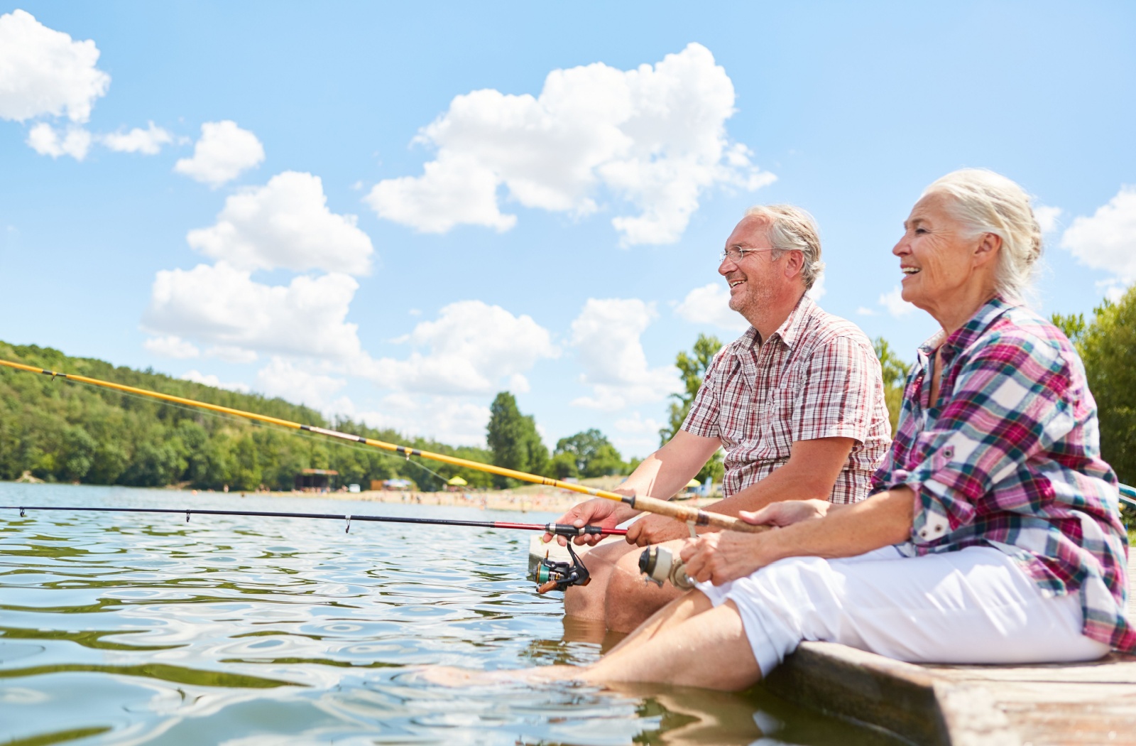 A senior couple fish together while sitting on a dock on a bright summer day in Ohio.