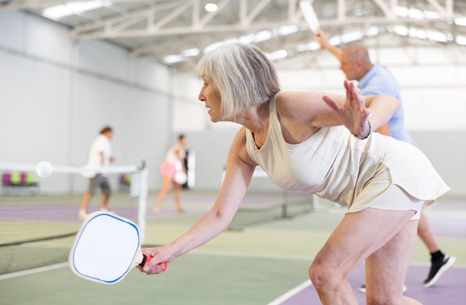 Two senior friends enjoy a game of pickleball on an indoor court with friends