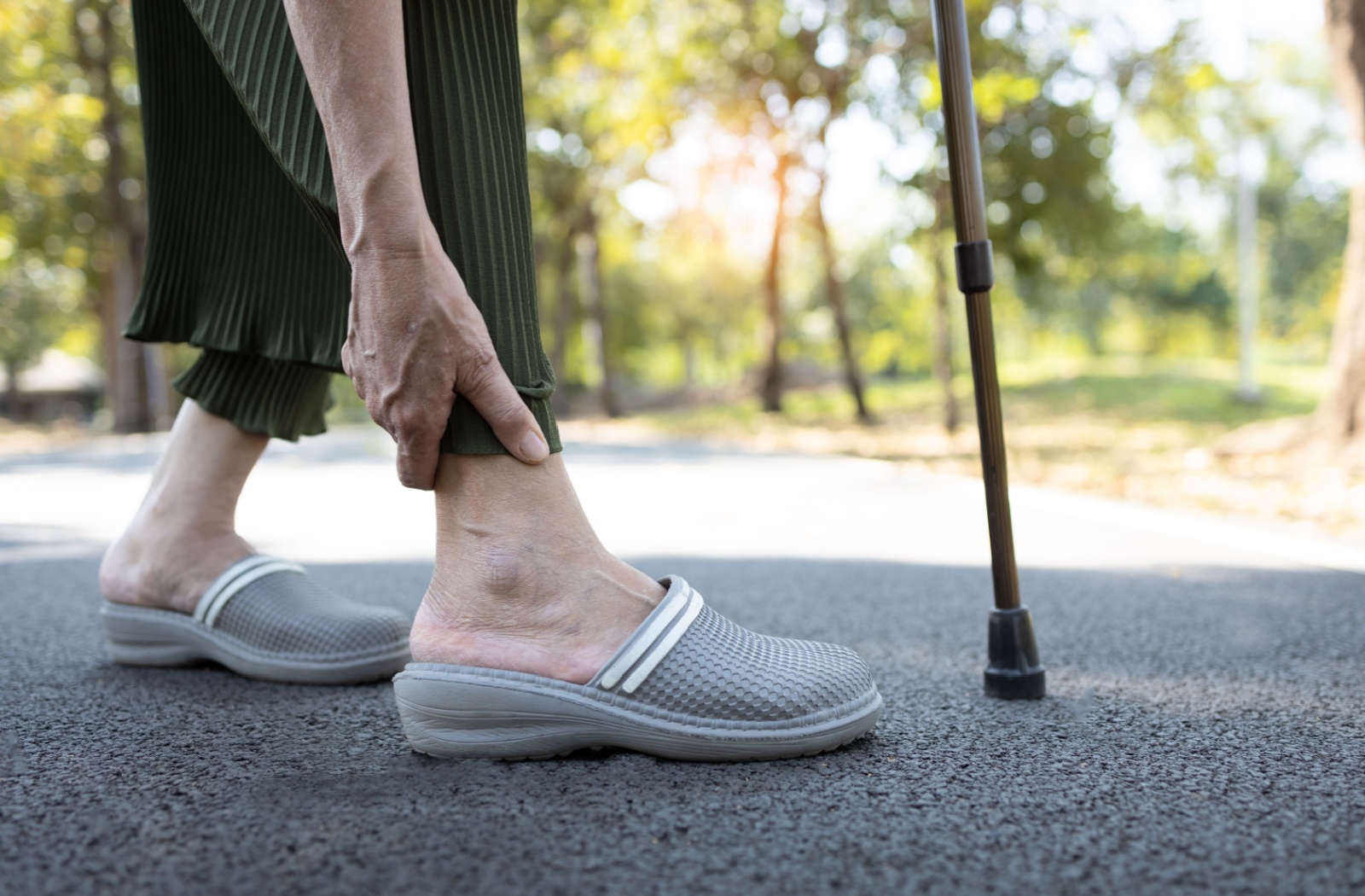 A senior reaches down to hold their ankle that is causing them pain.
