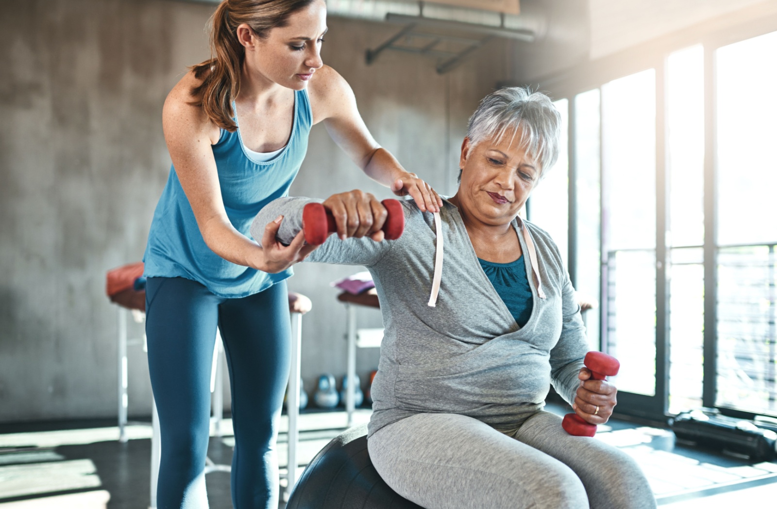 A senior uses light dumbbells to do arm-strengthening exercises, under the guidance of a caregiver
