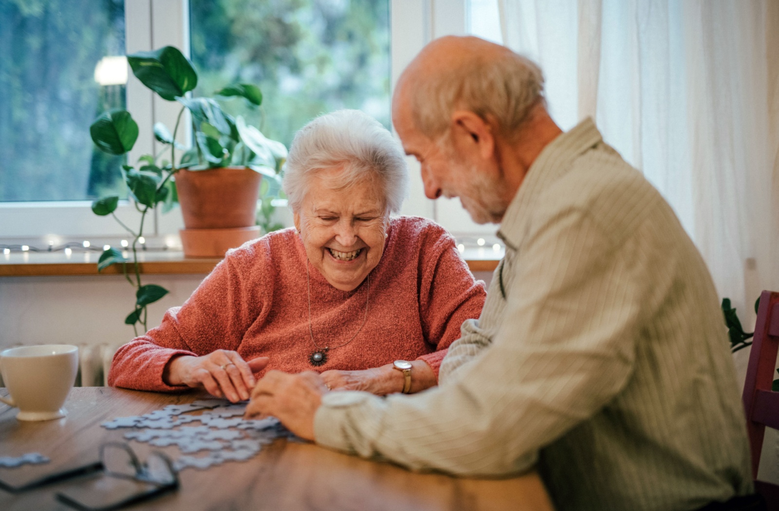 Two senior residents enjoy building a puzzle together at a table in a senior living community.
