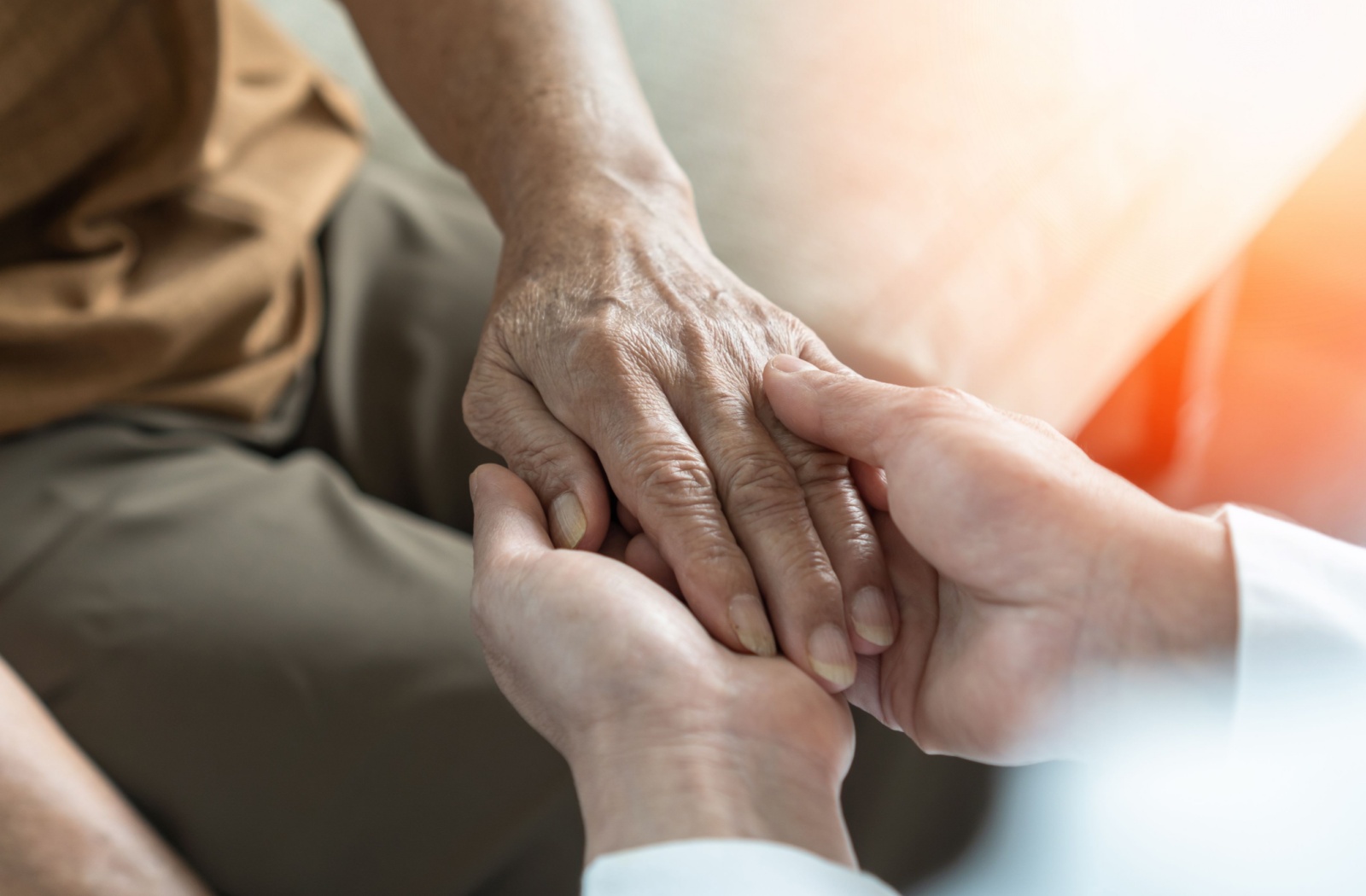 Close up of a younger caregiver holding the hand of a senior memory care resident.
