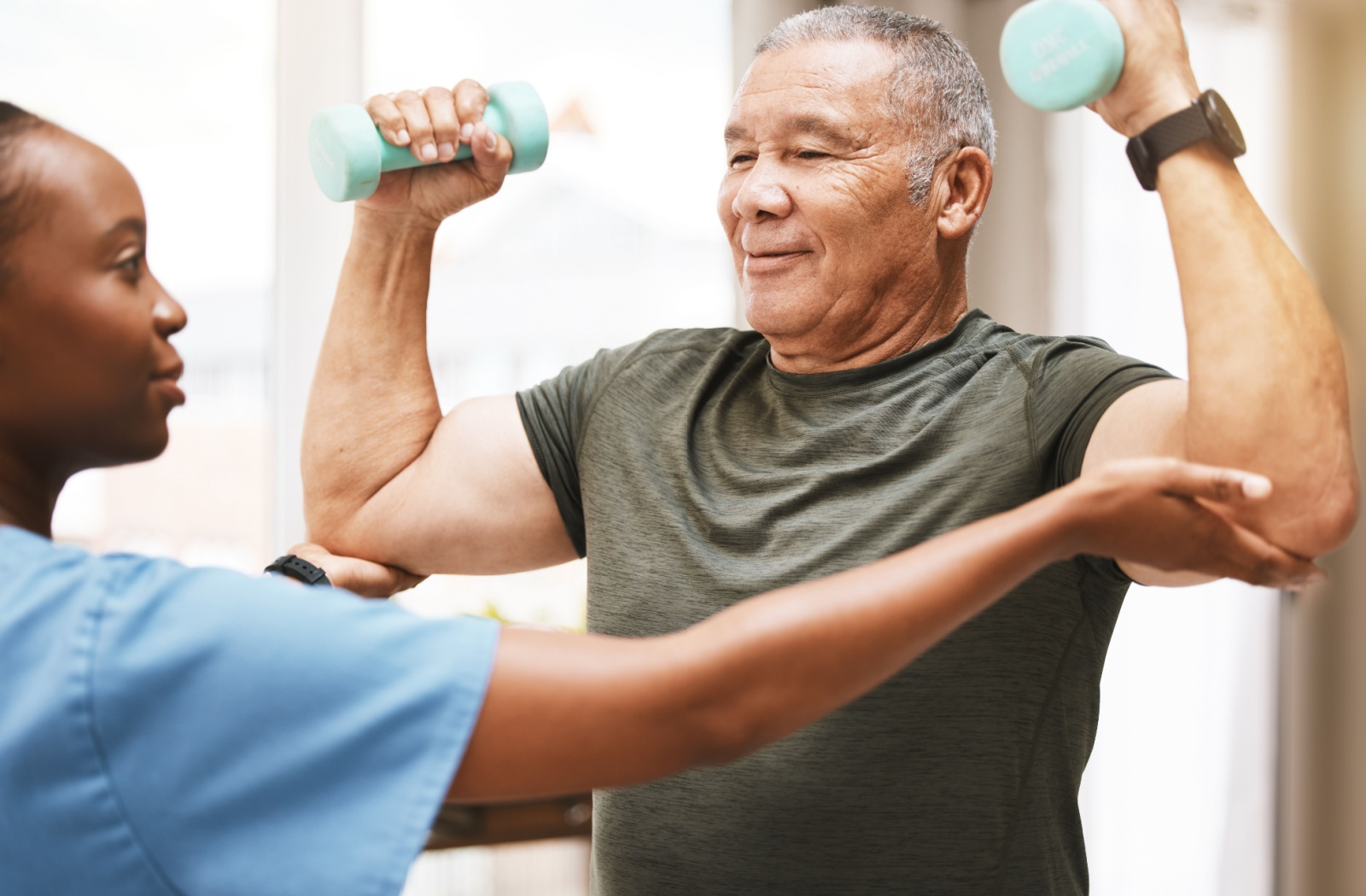 A senior resident uses light dumbbells to perform arm-strengthening exercises, under the supervision of a caregiver

