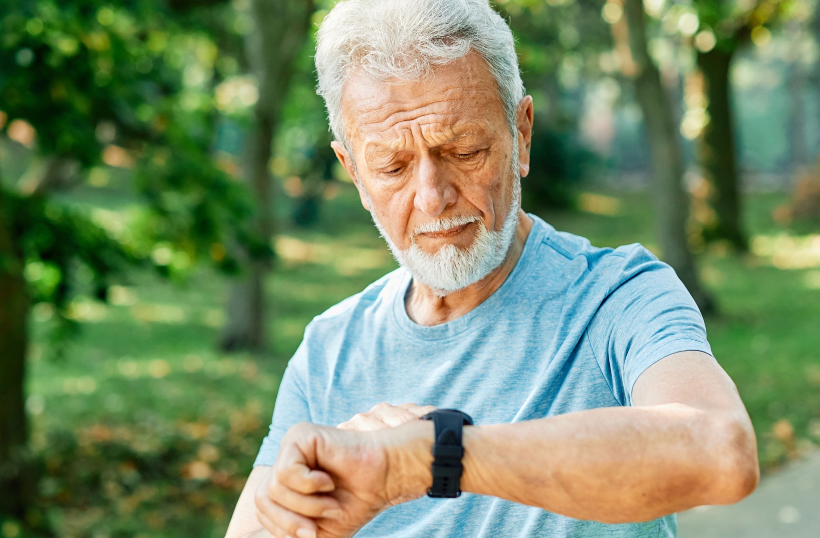 An older adult lifts a smart watch to their lips to activate voice command while sitting on a pale yellow sofa