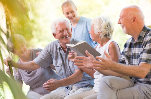 A group of senior friends smile together as one reads from a book.
