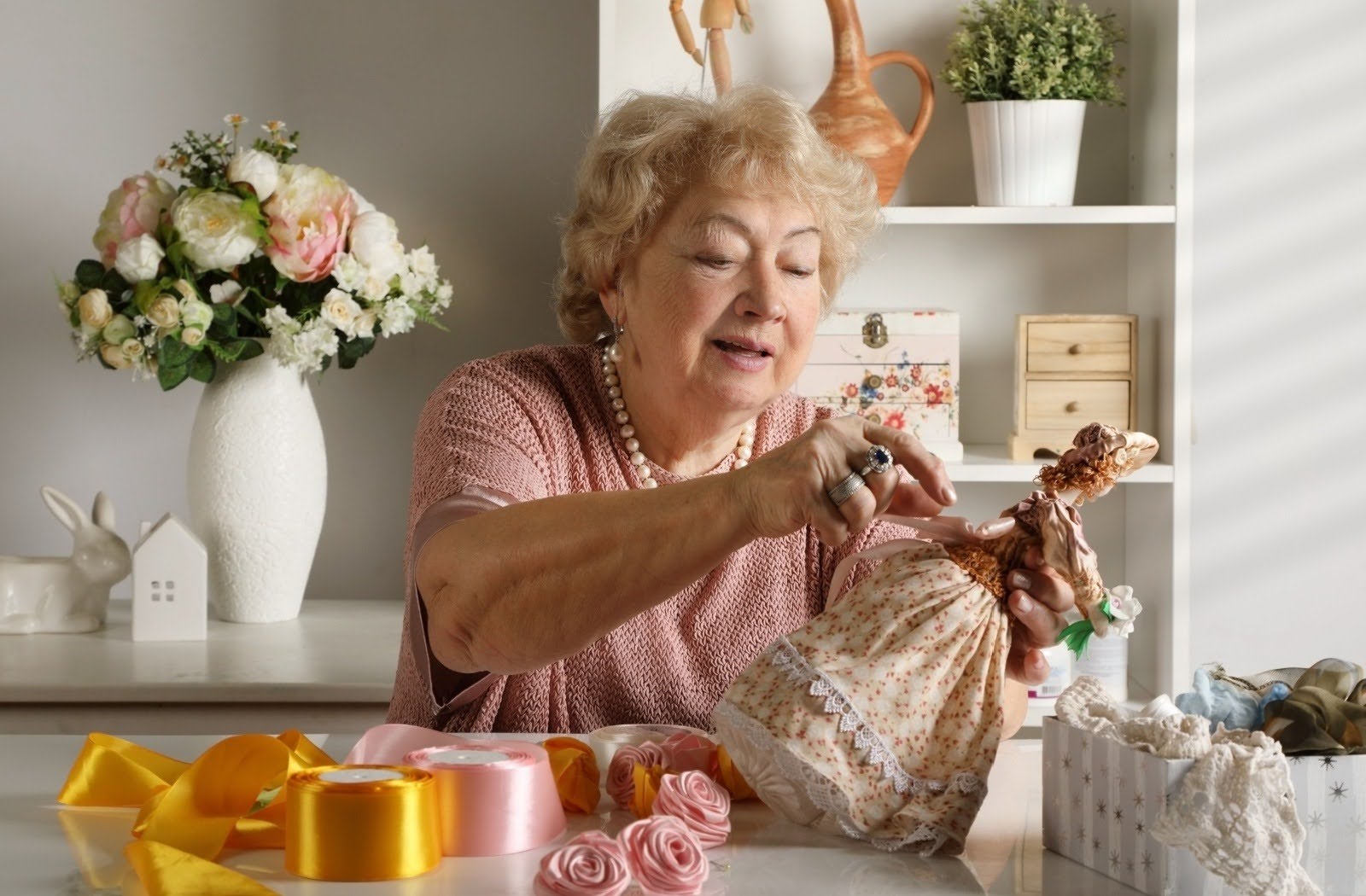 A senior resident creates ornate clothing for a doll using ribbon.
