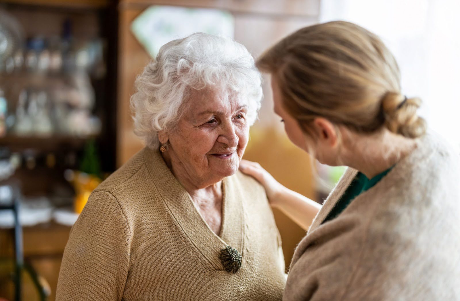 A senior with dementia smiles as they are comforted by a caregiver at a memory care community.
