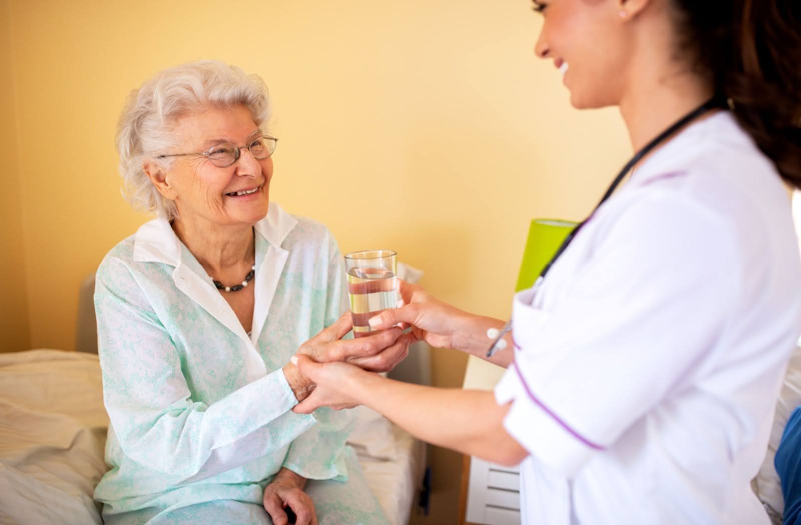 A nurse provides a smiling senior resident with a glass of water
