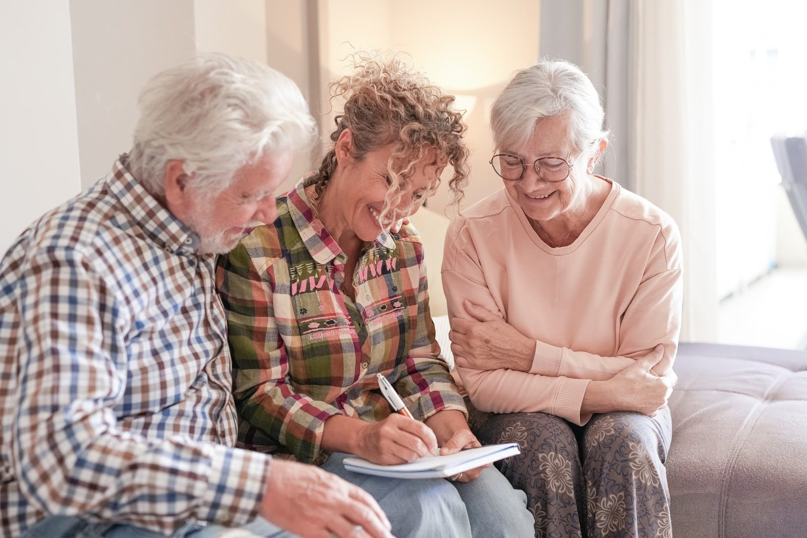 Smiling Senior couple and their daughter having a Moment sitting together on a sofa at home, smiling and having a discussion.