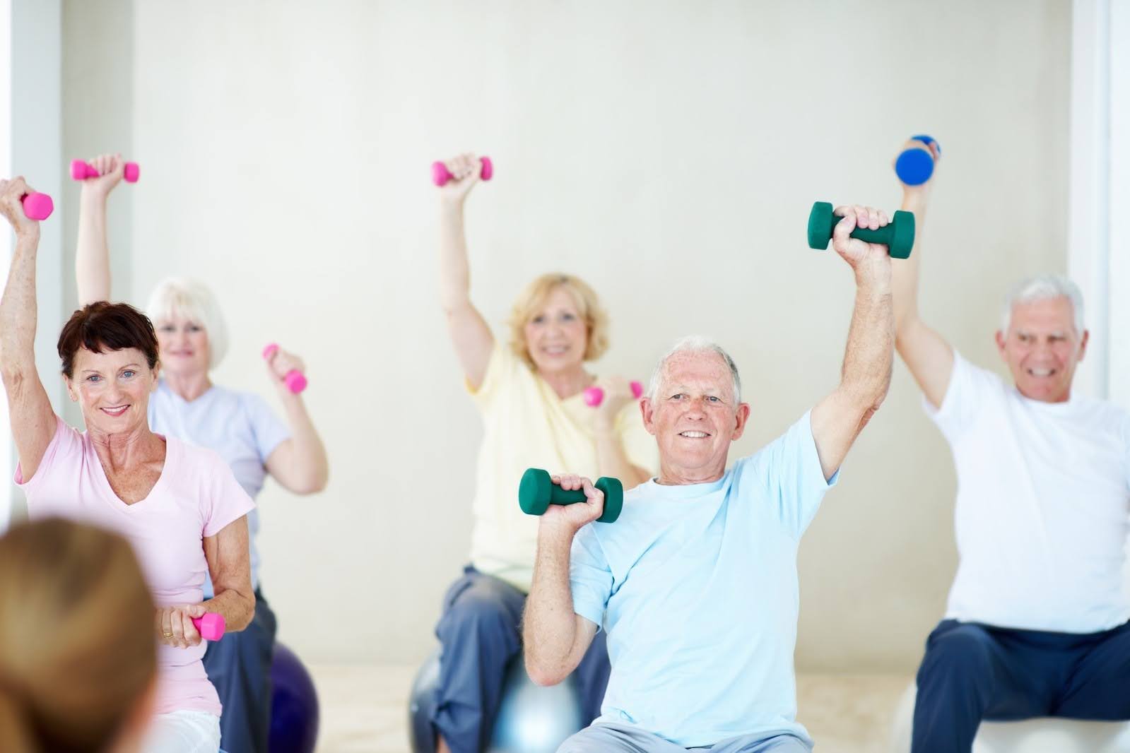 Dumbbells, exercise, and elderly people in gym class with personal trainer, workout, and retirement wellness.